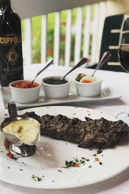 Grilled steak with a side of cream sauce, three small dipping sauces and a glass of red wine